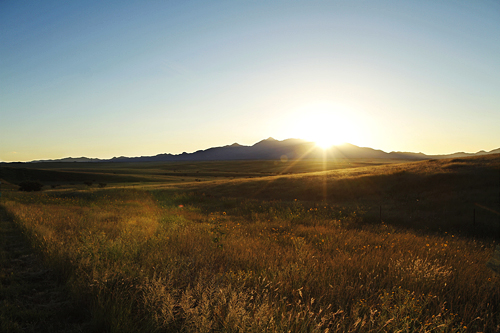The sun sets behind grassy, rolling hills and purple mountains a few miles west of Sonoita, AZ.